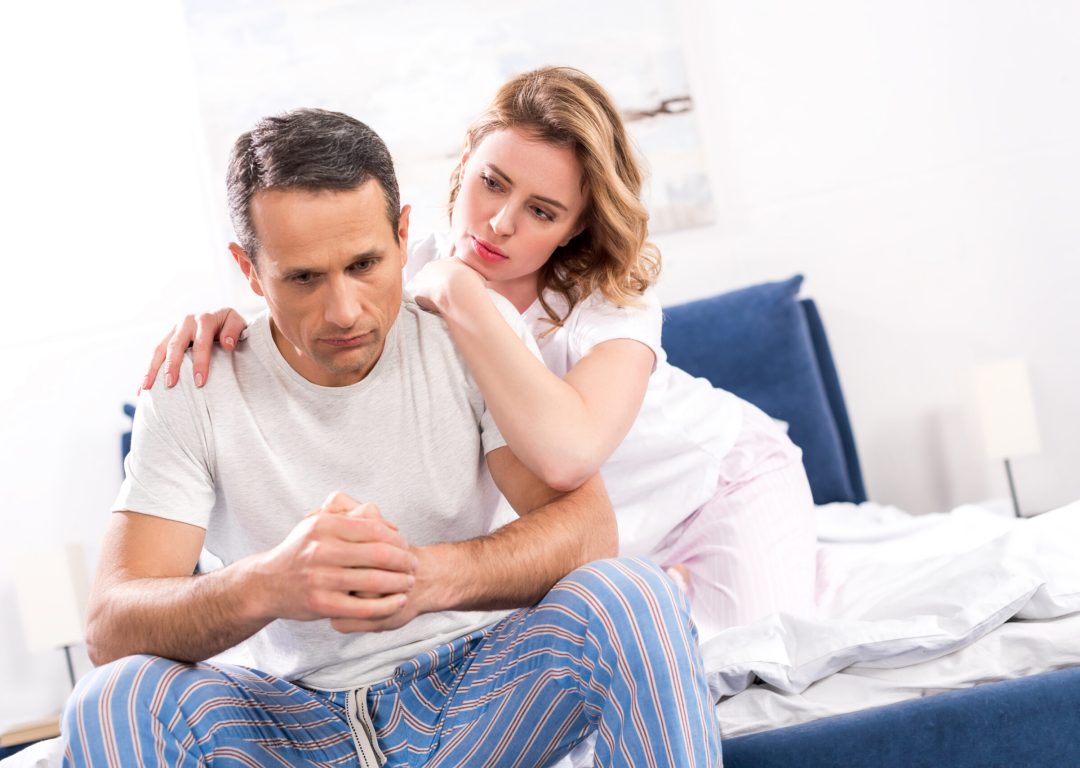woman hugging sad husband that sitting on bed at home